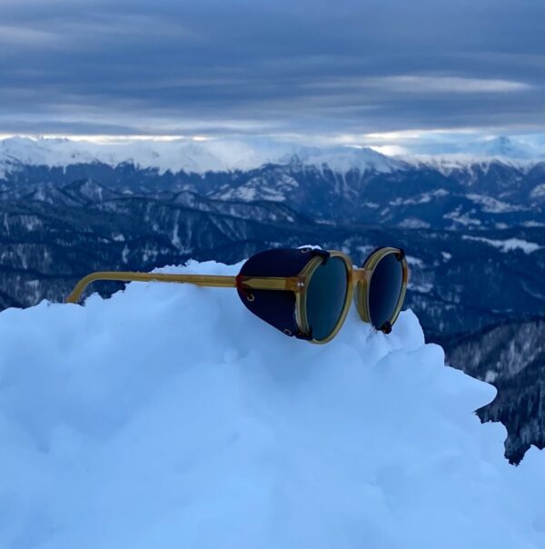 Protectores laterales extraíbles en color oscuro puestas en gafas de sol. Las gafas de sol se encuentran sobre la nieve. Los protectores laterales son de piel y se adapta a todos los modelos.
